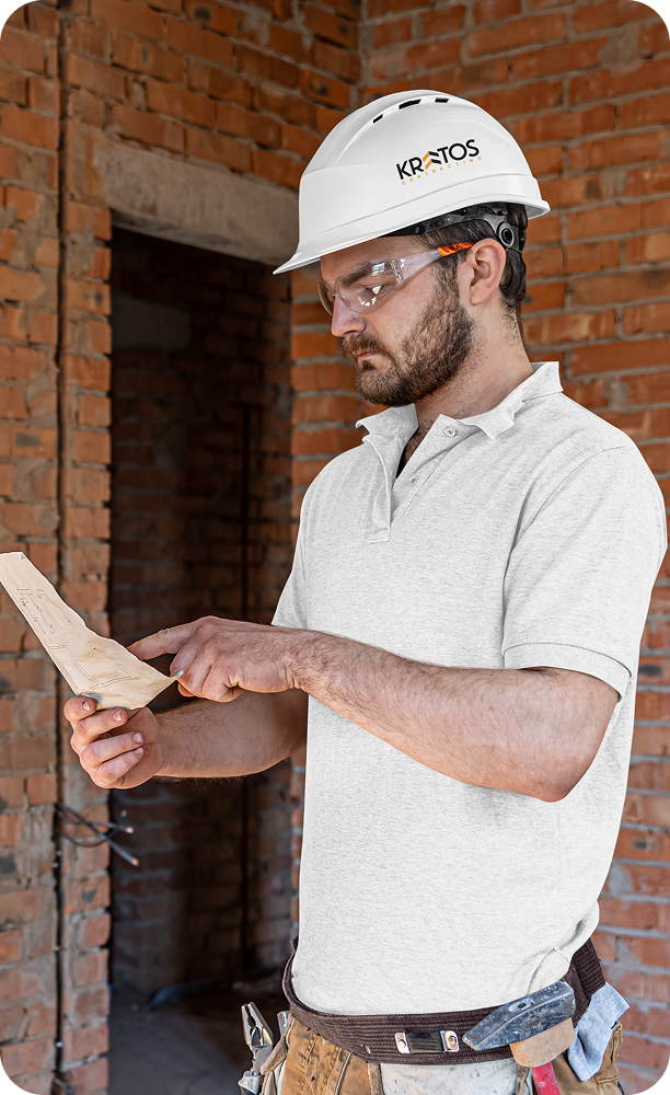 A professional Kratos Contracting project manager in a hard hat reviewing architectural blueprints on a construction site.